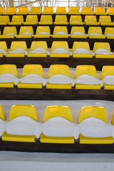 little football stadium tribune yelow chairs with winter snow