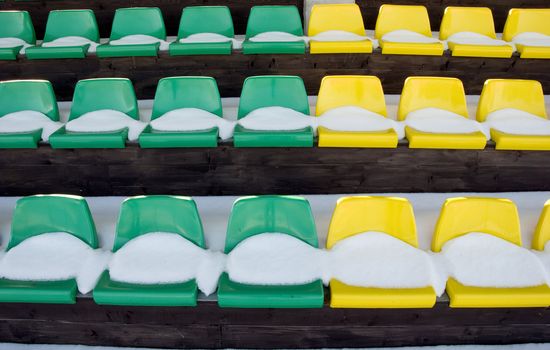 football stadium tribune yelow and green chairs with winter snow