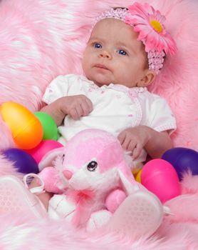 A cute infant girl on pink.  She has an easter bunny and a lot of easter eggs.