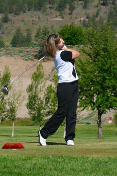 Blond female golfer following her ball from the tee-box