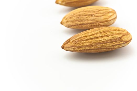 Three shelled almonds, in a row in right half of frame, on white background, with shadows.  Copy space to left.