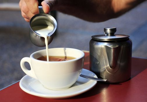 The man pours milk in tea