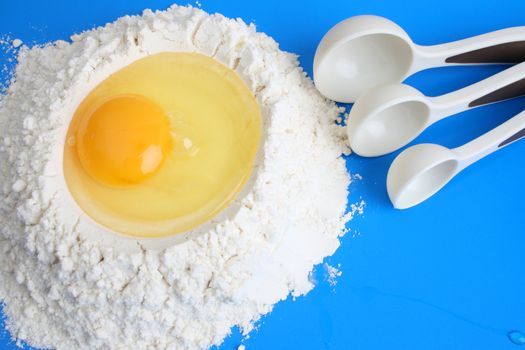 Raw egg in flower with measuring spoons, against a blue background
