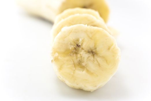 Close-up shot of banana slices in foreground, with remainder of peeled banana in soft focus in the background.  White background.