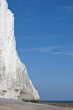 Portrait shot of a white chalk cliff at the sea's edge.  Sand, sea and blue sky visible.   Copy space.