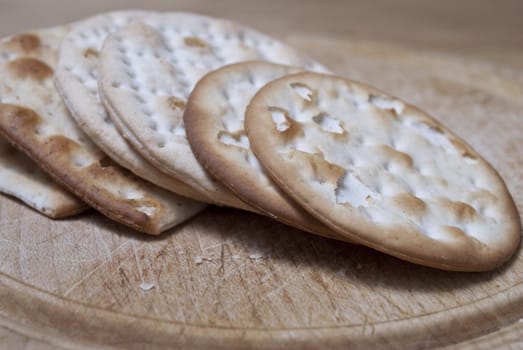 Closeup of crackers leaning against eachother on an old wooden chopping board, crumbs and cut marks visible.