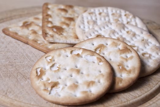 Closeup of a selection of square and round crackers (or 'biscuits') on wooden chopping board (cut marks visible).