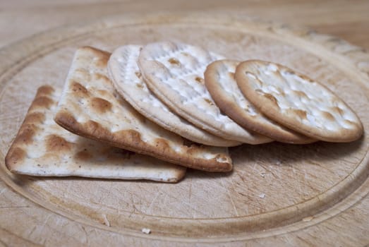 Selection of crackers on an old wooden chopping board, leaning against eachother.  Crumbs and cut-marks visible.  All crackers in-frame.