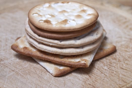 Closeup of a vertical stack of crackers on an old wooden chopping board, with cut marks visible.