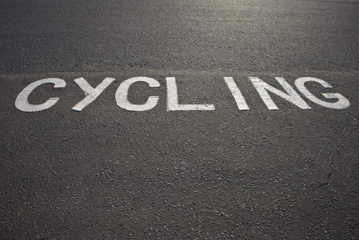 The word 'Cycling' painted in white on tarmac in winter sunlight.