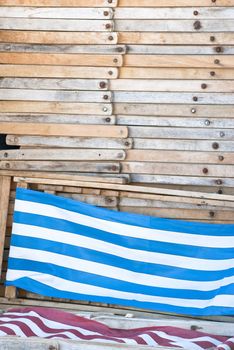 A pile of deckchairs, folded and stacked up.  The pile shows side views of the wooden frames, with two deckhairs at the bottom of the frame displaying their striped fabric.