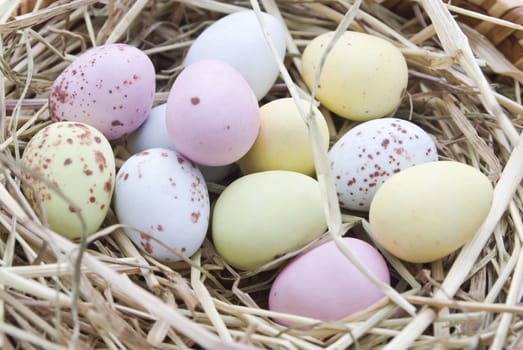Coloured, speckled eggs resting in a nest of straw. Pastel colours:  blue, yellow, pink and green.
