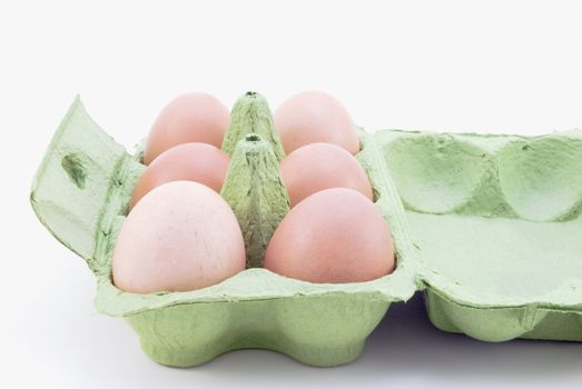 Half a dozen brown eggs in an opened green egg carton.  White background.