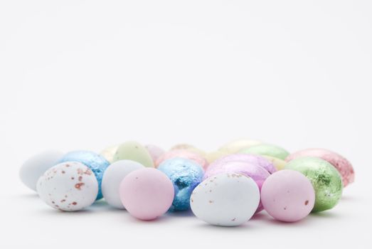 Eggs in coloured candy shells and eggs wrapped in tin foil grouped on a white surface.  Colours:  blue, pink, green, purple, gold, yellow.