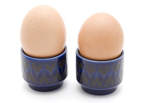 Two brown eggs in dark blue retro egg cups against white background.