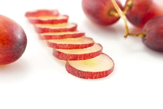 Close-up (macro) shot.  A single grape to the left, a line of moist grape slices leading towards the viewer, and a small bunch of three grapes in the upper right corner in soft focus.  White background.