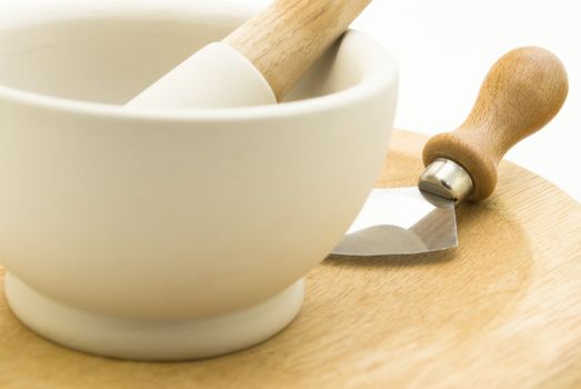 Close up of a cream stone pestle and mortar standing on a wooden mezzaluna chopping board with blade.  White background.