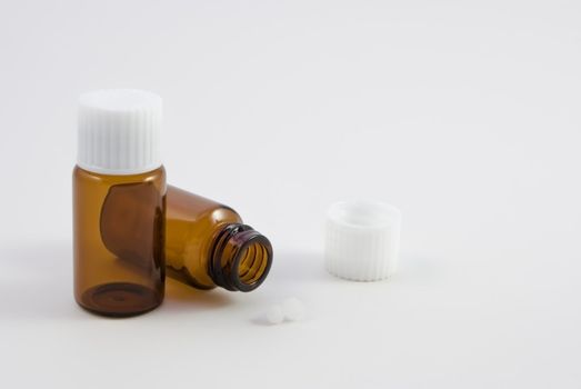 Two amber glass pill bottles, as used in homoeopathic pharmacy.  One upright, one tipped over, with two pills lying on the surface in front of it.