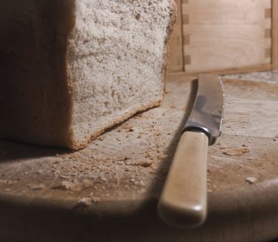 Loaf of bread on chopping board with knife and crumbs.  Rustic morning kitchen scene.