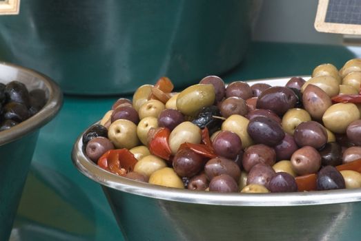 Two bowls of olives in foreground, one mixed and one black.  Sitting on a teal tablecloth on an open market stall.