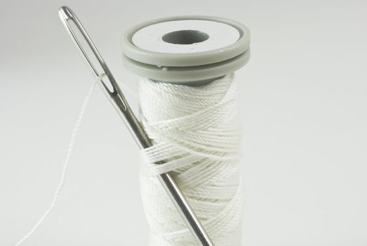 Sewing needle threaded with white cotton, inserted into thread on cotton reel.