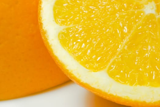 Close up (macro) of one slice of orange (quarter visible in foreground) leaning against upturned orange half, on white china surface with visible shadows.