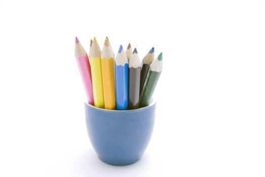 Set of coloured pencils in a blue ceramic container against a white background.  Pencil colours:  pink; red; yellow; green; orange/ochre; light blue; brown; black; dark blue; green.