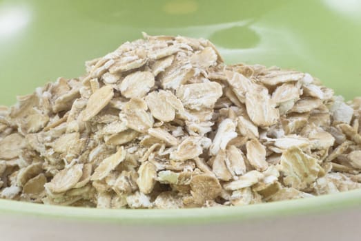 A cream bowl with a spring green interior, filled with dry porridge oats.