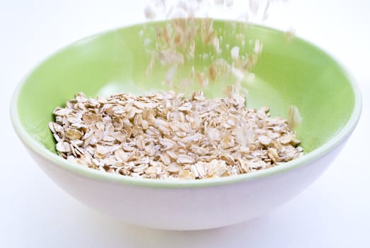 Action shot of dry porridge oats being poured into a cream coloured bowl with spring green interior. White background.