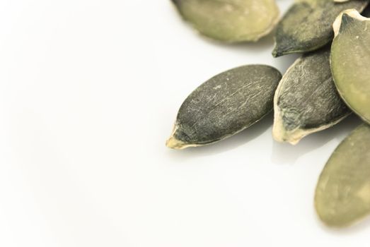 Closeup of pumpkin seeds emerging from right side of frame, with reflection showing on white china plate.  Copy space to the left.