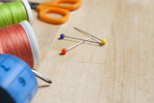 Close up of sewing items, cut off at left side of frame with three colourful pins in centre of frame.  These are placed on a birch wood table, which provides some copy space in areas containing no items.