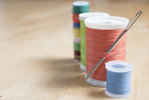 Close up of a row of cotton reels in a diagonal row on the right side of frame.  One cotton reel has a needle inserted into the thread body.  Lined up on a wooden birch table, with empty surface areas to the left to provide copy space.