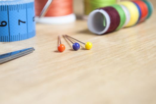 Close up shot of sewing tools on a birch wood table.  Scissors and pins in sharp focus, cottons, needle and measuring tape in background in soft focus.