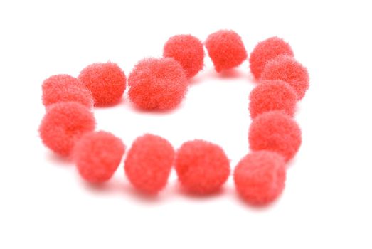 A heart shape made up from assembled red fluffy pompom balls.  White background.