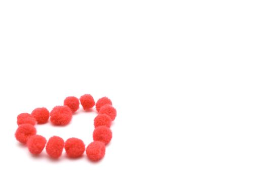 A heart shape made up from assembled red fluffy pompom balls, seated at
lower left of image.  White background with copy space.