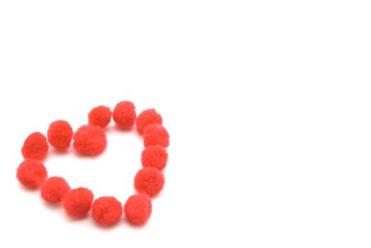 A heart shape made up from assembled red fluffy pompom balls. 
White background