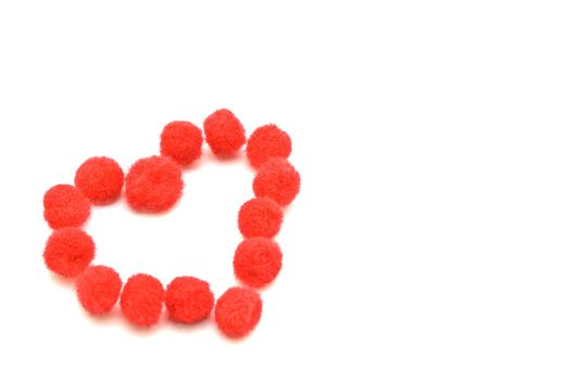 A heart shape made up from assembled red fluffy pompom balls. 
White background with copy space.