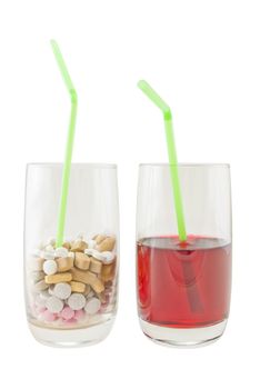 A glass of varied vitamin pills containing a green straw, next to a glass of red berry juice. Isolated against a white background.