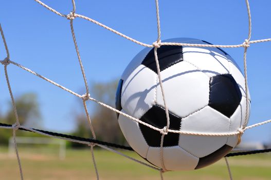 Closeup of soccer ball in net with goal in background.
