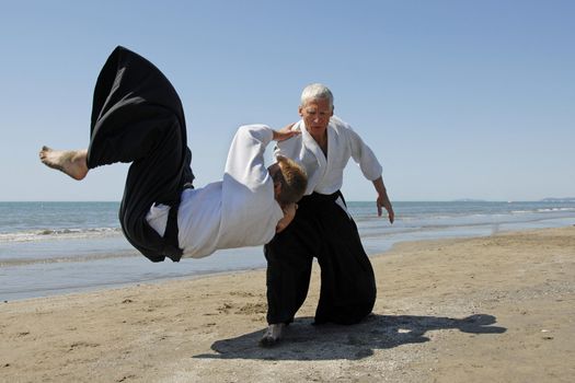 Two adults are training in Aikido on the beach