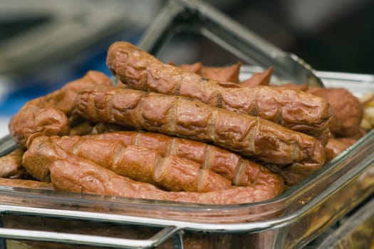 a glass tray with barbecued sauages in it with a pair of tongs in the background