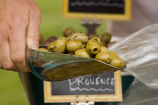a scoop of herb de provence olives being put into a bag for a customer at a market stall