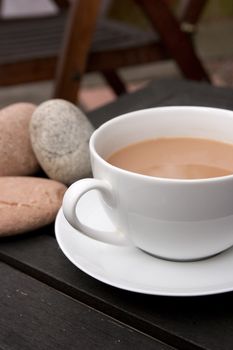 Outdoor cup of tea in a white cup and saucer with stones on a wooden background