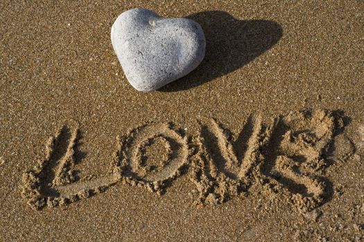 A heart shaped stone on a sandy beach with the word love under written in the sand
