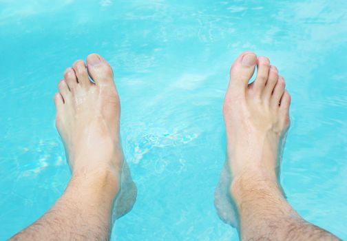 Two feet relaxing in the swimming pool water.