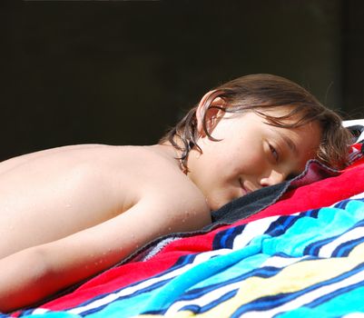 Teen boy lying down on a beach towel and sunbathing.