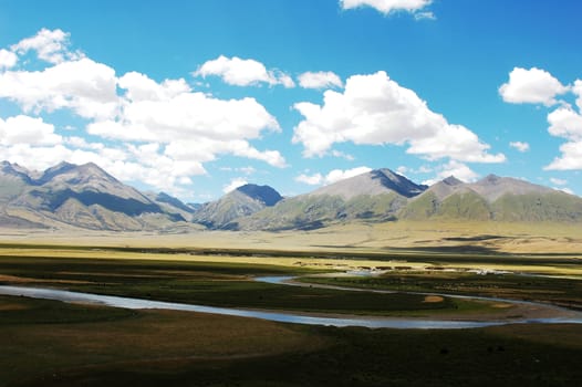 Landscape of mountains and meadows with a river under the blue sky and white clouds