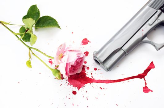 A pink rose with green stems and leaves, lying in a pool of red blood with the barrel of a gun visible. Set on a white background.