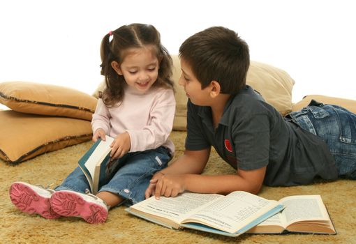 Brother and sister reading books over a carpet. They look interested and concentrated. 
