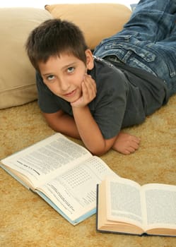 Boy in a room reading a book over a carpet. 